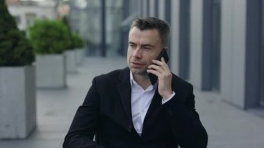 Klasik takım elbiseli olgun bir adamın açık havada telefon konuşması yapması. 40 'lı yıllardaki başarılı iş adamı, sokakta akıllı telefondan iletişim kurarken dinliyor. Meşgul insanlar kavramı..