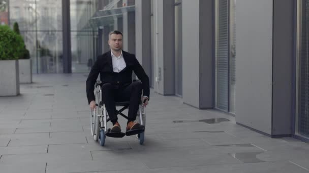 Серйозний інвалідний бізнесмен в костюмі дивиться вперед і в сторону під час виходу на вулицю. Успішний стильний чоловік їде на інвалідному кріслі біля офісної будівлі. Концепція мотивації . — стокове відео