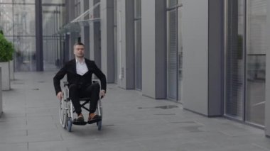 Sokakta yürürken önüne bakan tekerlekli sandalyedeki yakışıklı iş adamı. Ofis binasının yanındaki tekerlekli sandalyeye oturan başarılı ciddi bir erkek. Motivasyon kavramı, ızgara.