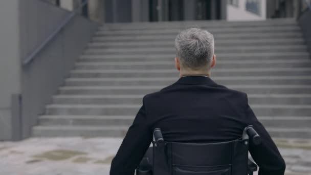 Vue de dos de la personne masculine en costume se poussant sur fauteuil roulant à la rue. Un handicapé va travailler et s'arrête près des escaliers de l'immeuble de bureaux. Notion d'obstacles, d'obstacles. — Video