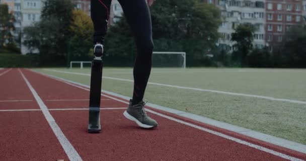 站在运动场上的带假肢跑步刀片的残疾男性的作物视图。被截肢的男子赛跑选手准备好了动机运动录像的概念. — 图库视频影像