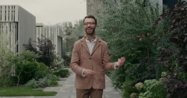 Gözlüklü ve fularlı mutlu bir adamın şehir caddesinde yürürken parmak şıklatması ve dans etmesi. Tarz sahibi sakallı adam heyecanlı görünüyor ve gülüyor..