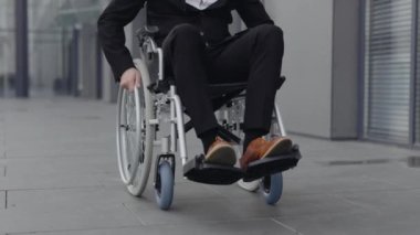 Şık ayakkabılı ve takım elbiseli bir erkeğin caddede tekerlekli sandalyeye oturması. Ofis binasının yakınındaki işe giderken başarılı bir erkek. Motivasyon kavramı, ızgara.