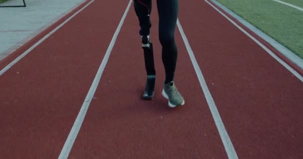 Vista de las piernas de hombre discapacitado con hoja protésica caminando en el campo de deportes. Atleta masculino discapacitado en pista al aire libre. Concepto de salud, deporte, red. — Vídeos de Stock