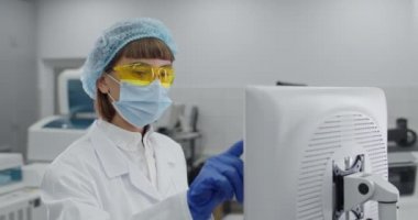 Koruyucu maskeli ve sarı Google 'lı bir kadın bilgisayar ekranına dokunup kaydırıyor. Beyaz elbiseli kadın bir bilim adamı araştırma merkezinde özel ekipmanlarla çalışıyor..