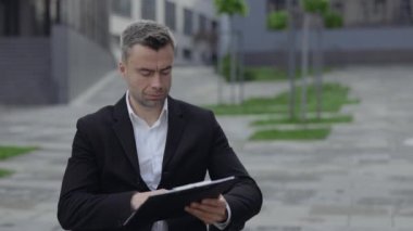 Şehir caddesindeki belgelere bakarken tekerlekli sandalyedeki başarılı adamın yakın görüntüsü. Ofis binası yakınlarında çalışırken resmi takım elbiseli ciddi bir işadamı engelli.