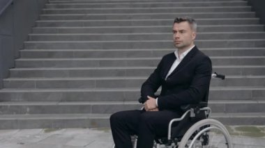 Sokakta tekerlekli sandalyede oturan klasik takım elbiseli ciddi bir iş adamının portresi. Engelli bir erkek kafasını çeviriyor ve dışarıya bakıyor. Yakınlaştır.