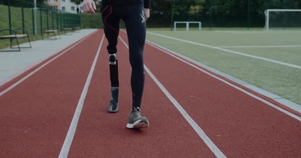 Vista de corte de pernas de pessoa masculina com deficiência com lâmina protética andando no campo esportivo. Atleta masculino deficiente em pista de corrida ao ar livre. Conceito de filmagens esportivas motivacionais. — Vídeo de Stock