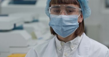 Koruyucu maske takan ve Google 'da kafasını çevirip kameraya bakan kadın görüntüsü. Laboratuvarda beyaz önlüklü ve kabarık şapkalı kadın doktorların vesikalık fotoğrafı. Araştırma kavramı..