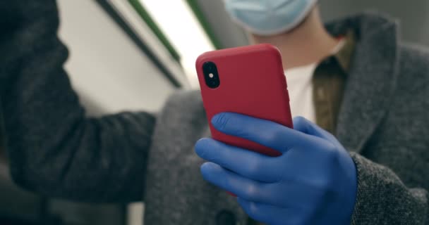 Vista de la cosecha de la persona masculina en máscara de protección médica y guantes de látex usando smartphone mientras va en transporte público. Concepto de paandemia, cuarentena. — Vídeos de Stock