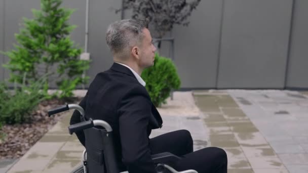 Vue de la récolte de la personne masculine en costume se poussant en fauteuil roulant dans la rue. Un handicapé va travailler et s'arrête près des escaliers de l'immeuble de bureaux. Notion d'obstacles, d'obstacles. — Video