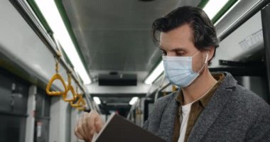 Tıbbi maskeli bir adamın otobüste kitap sayfalarını çevirmesi. Kablosuz kulaklıklar takan, hikaye okuyan ve toplu taşımada tırabzan tutan bir erkek. İşe gidip gelme kavramı.
