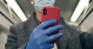 Tıbbi koruyucu maskeli ve lateks eldivenli bir adamın toplu taşıma araçlarında akıllı telefon kullanırken iç mekâna göz atması. Salgın, karantina kavramı.