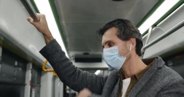 Tıbbi maskeli bir adamın öksürmesi ve otobüste hasta görünmesi. Kablosuz kulaklıklı bir erkek kendini kötü hissediyor ve toplu taşımada tırabzan tutuyor. Salgın, hastalık kavramı.