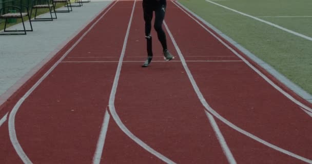 Crop view of disabled male person with prosthetic running blade at track on sport field. Amputé sportif masculin jogging. Concept de séquences sportives de motivation, paralympique. — Video