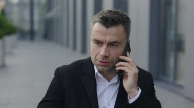 Klasik takım elbiseli, yakışıklı, olgun bir adamın açık havada telefon konuşması yapmasını yakından izleyin. 40 'lı yıllardaki başarılı iş adamının portresi sokakta akıllı telefondan iletişim kurarken dinliyor..