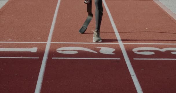 Вид на урожай спортсмена-инвалида с протезной ногой, бегущего по трассе на открытом спортивном стадионе. Мужчина с ампутированной ногой в стартовой гонке. Концепция спорта, паралимпийские игры, мотивация. — стоковое видео