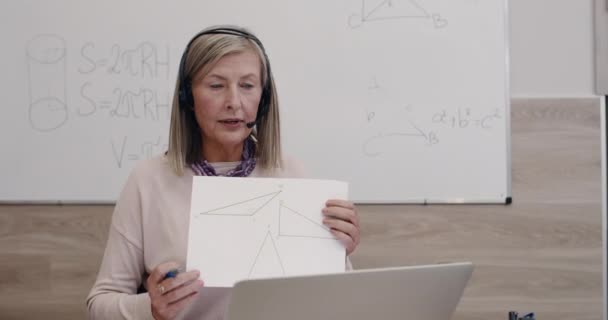 Primo piano di insegnante di sesso femminile parlando e mostrando triangoli durante l'utilizzo del computer portatile. Donna in cuffia con microfono che insegna matematica seduta alla scrivania. Concetto di apprendimento a distanza. — Video Stock