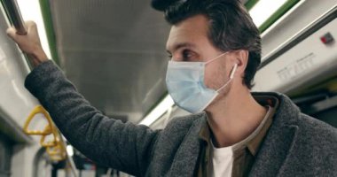 Akıllı telefon kullanarak koruyucu tıbbi maske takan yakışıklı adama yaklaş. Kablosuz kulaklıklı, müzik dinleyen ve yeraltında tırabzan tutan bir erkek. Salgın kavramı.