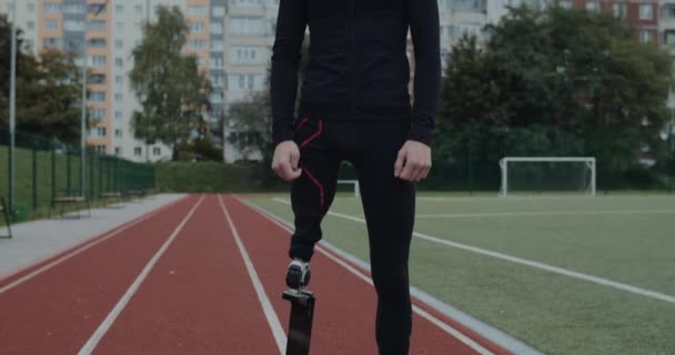 Портрет молодого человека-инвалида с протезным бегущим лезвием, стоящим на спортивной площадке. Позитивный спортсмен-ампутант смотрит в камеру на улице. Концепция мотивационных спортивных кадров. — стоковое видео