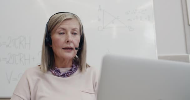 Vista da vicino della bellissima professoressa in cuffia wireless con microfono mentre guarda lo schermo del computer portatile. Donna matura avendo lezione online. Concetto di apprendimento a distanza. — Video Stock