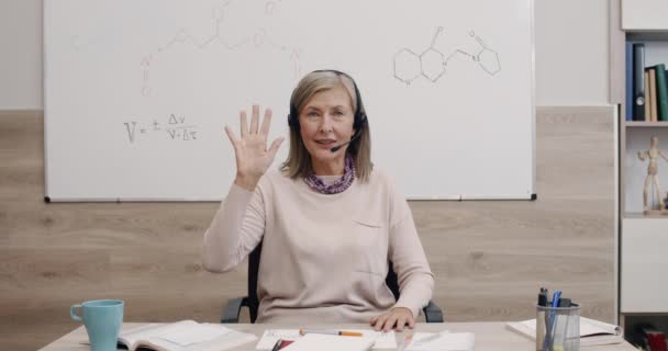 Crop vista di donna matura allegra agitando e parlando mentre si guarda alla fotocamera. Professoressa in cuffia con microfono che spiega materiale mentre ha lezione. Concetto di apprendimento online. — Video Stock