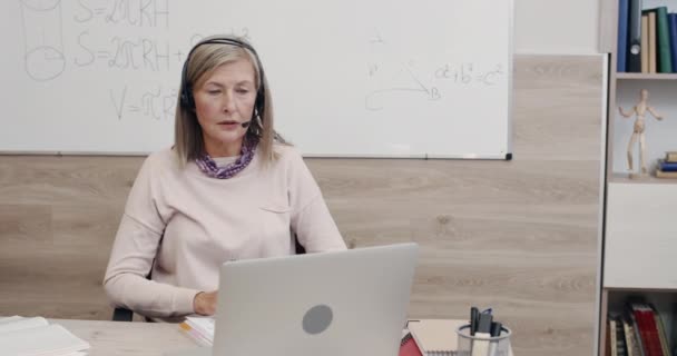 Vista ritagliare di professore femminile positivo in auricolare wireless con microfono parlando mentre guardando lo schermo del computer portatile. Donna matura avendo lezione online. Concetto di apprendimento a distanza. — Video Stock