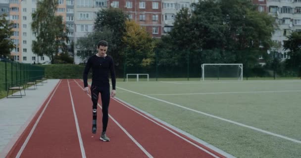 Hombre de espíritu fuerte discapacitado con prótesis que corre por la pista. Joven deportista masculino con pierna amputada que parece cansado en el campo de deportes. Concepto de salud, deporte, red. — Vídeo de stock