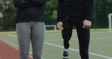 Bilinmeyen kadın ve sakat adamın spor sahasında duran protez bacaklı görüntüsü. Eğitimli kadın ve erkek açık havada takım elbise giyiyor. Destek kavramı.