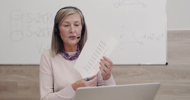 Großaufnahme einer Grundschullehrerin, die mit Laptop redet und Einmaleins zeigt. Frau mit Kopfhörer und Mikrofon, während sie am Schreibtisch sitzt. Konzept des Fernstudiums. — Stockvideo