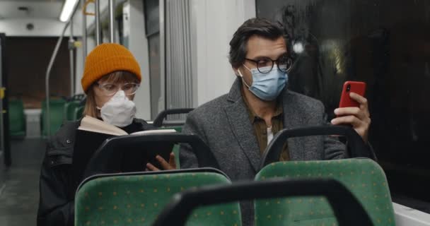 Žena s knihou vstane a odejde, když muž sedící vedle ní v tramvaji začne kašlat. Lidé v lékařských maskách dojíždějící veřejnou dopravou. Koncepce pandemie, nemoci, karantény. — Stock video