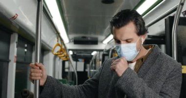 Crop view of man in medical mask having cough and looking ill in tram. Male person in wireless earbuds feeling bad and holding handrail in underground. Concept of pandemic, illness.