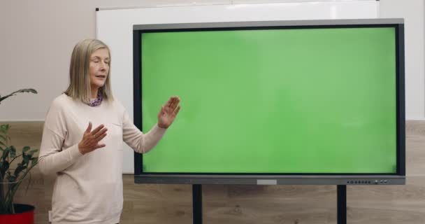 Kluge Frau spricht, während sie interaktiven Bildschirm mit Vorlage Green Screen benutzt und berührt. Professorin erklärt Material und blickt in die Kamera, während sie in der Nähe von digatal board steht. — Stockvideo