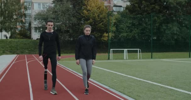 Junge Frau und behinderter Mann beim Gehen und Positionieren auf Markierungen am Start. Weibliche und männliche Athleten mit Laufklinge vor dem Lauf auf der Rennstrecke im Stadion. Konzept des Sports. — Stockvideo