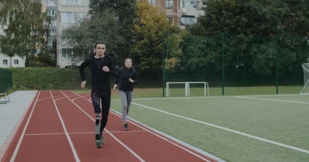 Motivierte Behinderte überholen Sportlerin beim Joggen. Ein männlicher Athlet mit Laufklinge und eine weibliche Person laufen auf der Rennstrecke im Stadion. Konzept von Motivation, Gesundheit, Sport. — Stockvideo