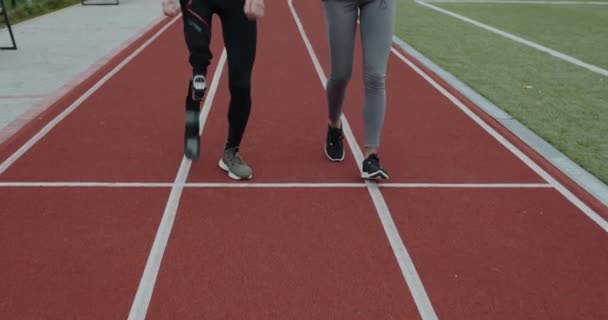 Crop view of disabled man and sports woman jogging. Male athlete with running blade and female person run on race track at stadium. Concept of motiation, health, sports. — Stock Video