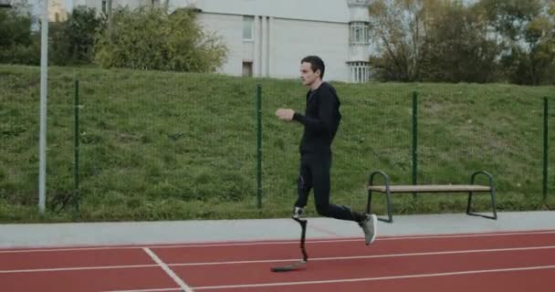 Seitenansicht eines behinderten männlichen Sportlers mit amputiertem Bein beim Joggen auf dem Sportplatz. Behinderte männliche Athleten auf der Laufbahn im Freien. Konzept Gesundheit, Sport, Raster. — Stockvideo