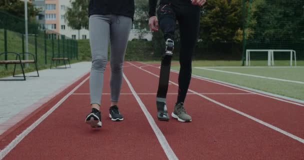 Вид на урожай неизвестной женщины и инвалида с протезной ногой на спортивной площадке. Мужчина и женщина в тренировочных костюмах идут на беговую дорожку. Концепция мотивации и поддержки. — стоковое видео