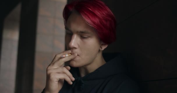 Lviv, Ucrania - 25 de julio de 2019: Joven en depresión fumando cigarrillos y pensando. Millennial hipster persona con el pelo teñido de rojo y pendiente mirando a un lado mientras está de pie en la calle urbana. — Vídeos de Stock