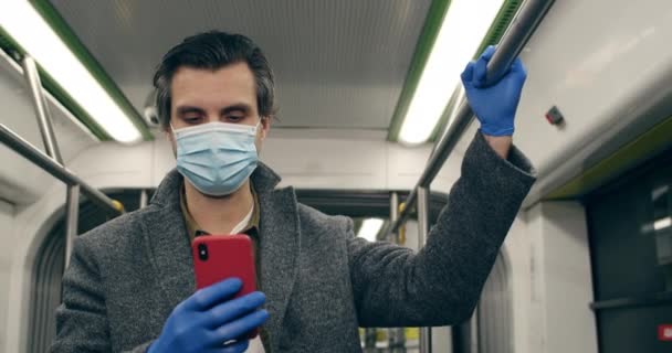 Вид на людину в захисній медичній масці та латексних рукавичках за допомогою смартфона. Чоловік в навушниках друкує повідомлення і спілкується в громадському транспорті. Концепція пандемії, карантину . — стокове відео
