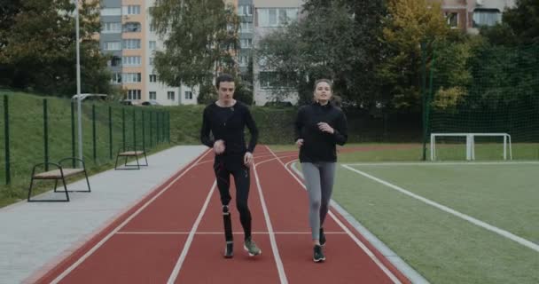 Disabled man with amputated leg and sports woman jogging. Male sportsman with running blade and female person run on race track at stadium. Concept of motiation, health, sports. — Stock Video