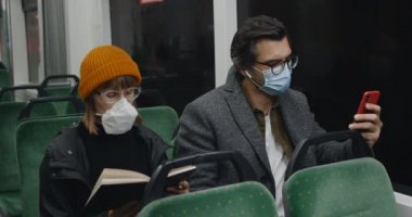 Akıllı telefon kullanan adam, yanında oturan kadın ayağa kalkıp uzaklaşırken öksürmeye başladı. Tıbbi maskeli insanlar toplu taşıma araçlarında seyahat ediyorlar. Salgın, hastalık kavramı.