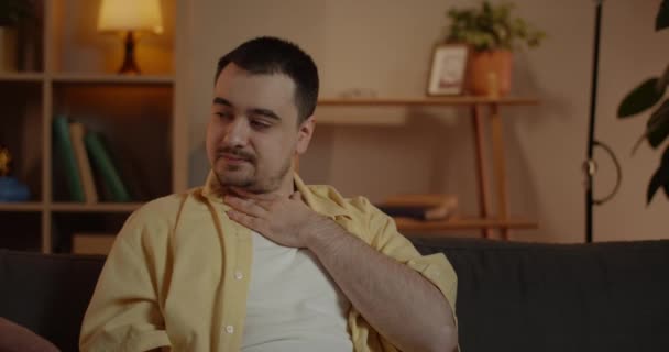 Gość od upraw źle wygląda. Mężczyzna rasy kaukaskiej chory i cierpiący na ból gardła podczas siedzenia na kanapie w domu.Pojęcie zdrowia ludzi, choroby, wirusy. — Wideo stockowe