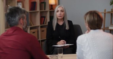 Evli bir çiftle seans yaparken elinde karton olan kadın psikoloğun ön görüntüsü. Olgun bir kadın müşterileriyle aile sorunlarını tartışıyor. İlişki kavramı.