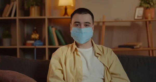 Portrait of guy in medical protective mask turning head and looking to camera. Crop view of male adult person sitting at home. Concept of quarantine, viruses, health prevention. Stock Image