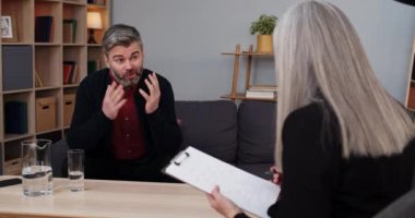 Duygusal bir adamın kadın ile oturduğu ve terapi gördüğü bir manzara. Kadın terapist notlar alırken erkek sakallı adam sorunlardan ve hareketlerden bahsediyor..