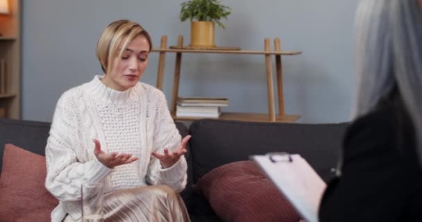 Vista da cultura da jovem mulher emocional conversando com seu terapeuta e gesticulando no escritório. Mulher loira cabelo pessoa sentada na frente do psicólogo na sessão de terapia. Conceito de problemas de pessoas. — Vídeo de Stock