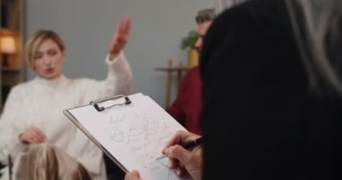 Kartonla yazı yazan kadın psikolog evli bir çiftle otururken aile sorunlarını tartışıyor ve kanepede otururken birbirlerine bağırıyorlar..
