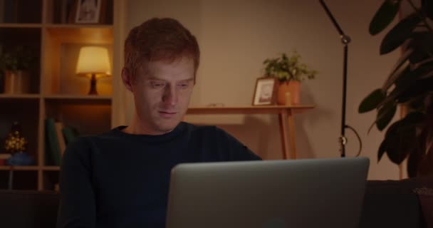 Crop view of handsome red haired man using laptop while sitting on sofa at home.Young guy browsing internet and looking at computer screen.Concept of free time and leisure. — Stock Video