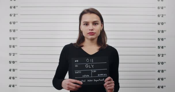 Een politiefoto van een aantrekkelijke jonge vrouw met een uithangbord. Crop view van mooie brunette vrouwelijke crimineel poseren, het verhogen van het hoofd en op zoek naar camera. — Stockvideo